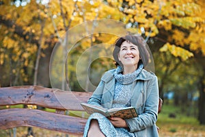 Senior woman is reading the book and dreaming in the park