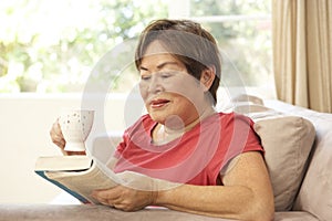 Senior Woman Reading Book With Drink At Home