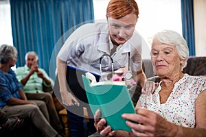 Senior woman reading book with nurse