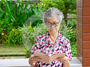 Senior woman reading a book while sitting on a balcony. Space for text. Concept of aged people and healthcare