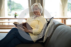 Senior woman reading book on sofa in living room
