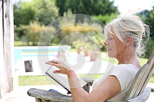 Senior woman reading book by the swimming pool