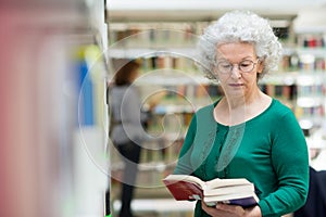 Senior woman reading and choosing book in library