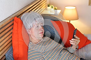 Senior woman reading on her phone in bed