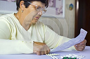 Senior woman reading information sheet of prescribed medicine sitting at table at home