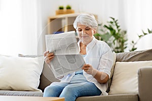 Senior woman reading newspaper at home