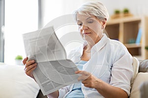 Senior woman reading newspaper at home