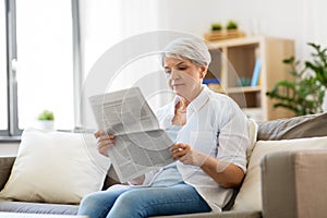 Senior woman reading newspaper at home