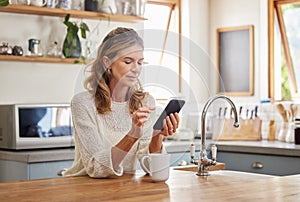 Senior woman reading phone news, mobile apps and social media notification in morning home kitchen. Relax retirement