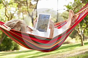 Senior Woman Relaxing In Hammock With E-Book