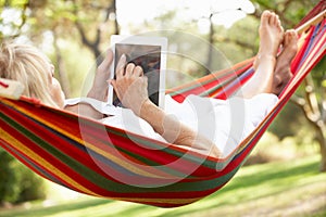 Senior Woman Relaxing In Hammock With E-Book