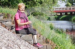 Senior woman resting after nordic walking on riverside, sporty lifestyles