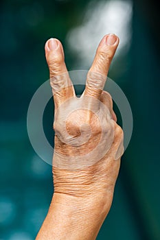 Senior woman right hand raise two fingers up in bokeh blue swimming pool background, Close up, Gesturing, Body Language