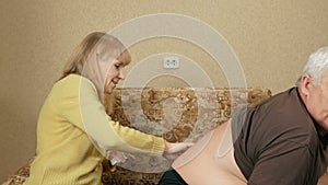 Senior woman rubs ointment for back pain man overweight. Husband picked up a T-shirt and tolerate pain.