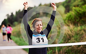 Senior woman runner crossing finish line in a race competition in nature.