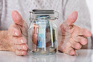 Senior Woman`s Hand Protecting Money Jar