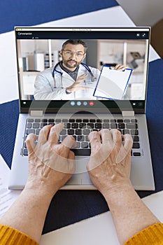 Senior woman`s hands behind the laptop keyboard. Online consultation with your doctor. Vertical photo.