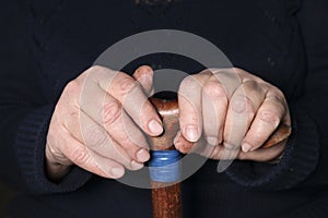 Senior woman`s hands on old walking stick with t shaped handles. The concept of old age, loneliness, solicitude and caring