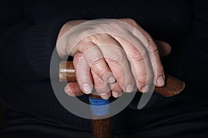 Senior woman`s hands on old walking stick with t shaped handles. The concept of old age, loneliness, solicitude and caring