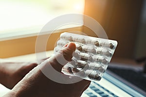 Senior woman`s hands typing on laptop holding pills at home, online doctor medical help for senior people