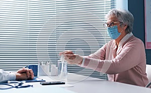 Senior woman sanitizing her hands in the doctor`s office