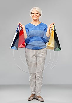 Senior woman with shopping bags over grey