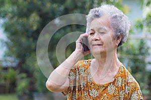 A senior woman with short gray hair using a smartphone while standing in a garden. Space for text. Concept of aged people