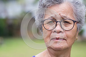 Senior woman with short gray hair wearing glasses and looking at the camera while standing in a garden. Concept of aged people