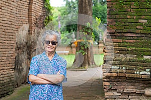 Senior woman with short gray hair wearing sunglasses, arms crossed, smiling, and looking at the camera while standing