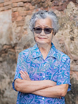 Senior woman with short gray hair wearing sunglasses, arms crossed, smiling, and looking at the camera while standing