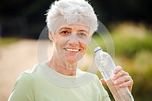 Senior woman with short grey hair drinking water after exercising, portrait in the park