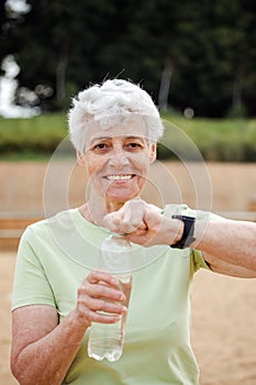 Senior woman with short grey hair drinking water after exercising, portrait in the park