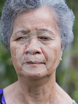 Senior woman with short white hair, anxious face, and looking away while standing in a garden. Concept of old people and