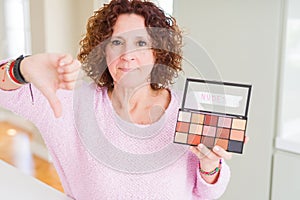 Senior woman showing nudes eyeshadows colors with angry face, negative sign showing dislike with thumbs down, rejection concept