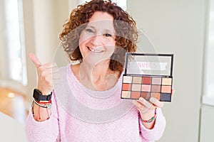 Senior woman showing nudes eyeshadows colors pointing and showing with thumb up to the side with happy face smiling