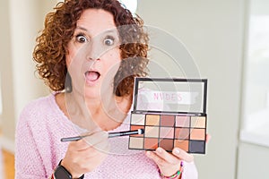 Senior woman showing nudes eyeshadows colors scared in shock with a surprise face, afraid and excited with fear expression