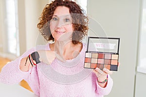Senior woman showing nudes eyeshadows colors with surprise face pointing finger to himself