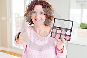 Senior woman showing palette of pink blush happy with big smile doing ok sign, thumb up with fingers, excellent sign