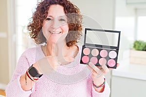 Senior woman showing palette of pink blush very happy pointing with hand and finger