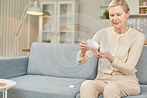 Senior woman sit on couch having daily vitamins or diet supplements at home, mature old female pensioner take dose of pills from