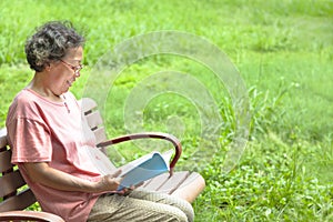 Senior woman sitting on bench and reading a book