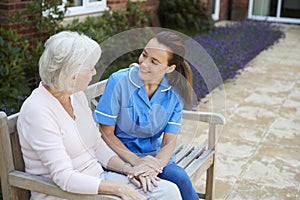 Senior Woman Sitting On Bench And Talking With Nurse In Retirement Home