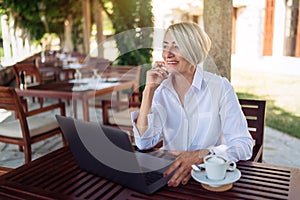 Senior woman sitting at a cafe with laptop computer