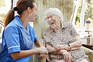 Senior Woman Sitting In Chair And Laughing With Nurse In Retirement Home photo