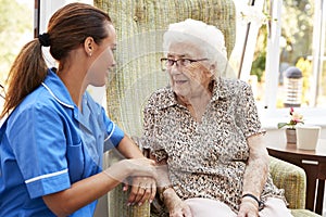 Senior Woman Sitting In Chair And Talking With Nurse In Retirement Home