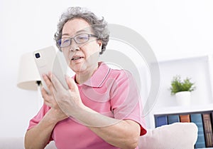 Senior woman sitting on couch and browsing mobile phone