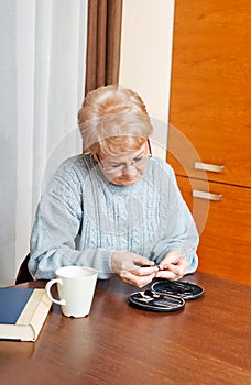 Senior woman sitting at the desk and cutting fingers nails