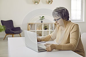 Senior woman sitting at desk and using her laptop computer for remote work or studying