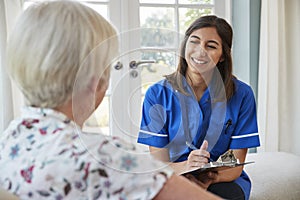 Senior woman sitting at home with care nurse taking notes