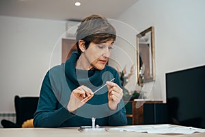 Senior woman sitting at home, studying the instructions for a self test for COVID-19
